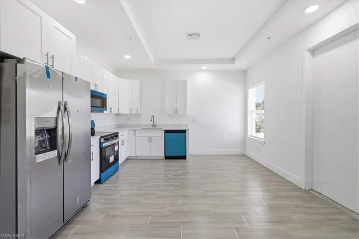 Bright kitchen featuring white shaker cabinetry, stainless steel appliances, light-toned tile flooring, recessed lighting, and tray ceiling detailing