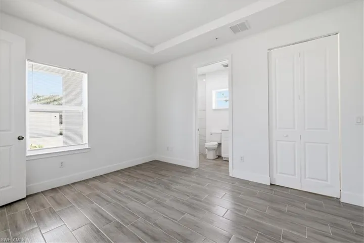 Recessed tray ceiling, plank-style tile flooring, white trim, white paneled doors, and a window with horizontal blinds