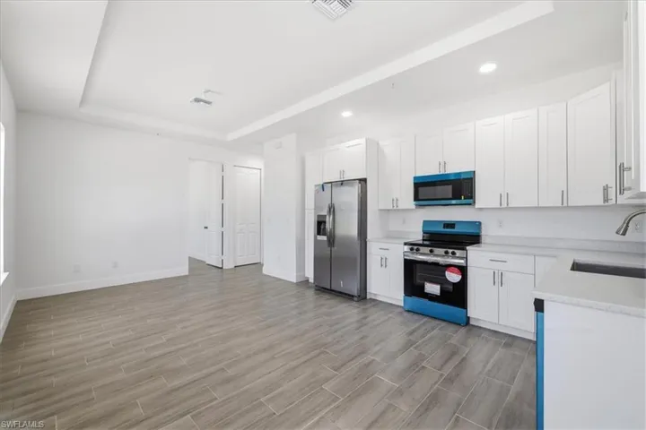 Modern kitchen featuring white shaker cabinetry, stainless steel appliances, light countertops, and wood-finish tile flooring