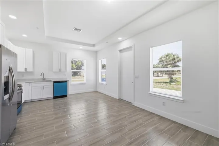 Open-concept living area featuring a kitchen with white cabinetry, stainless steel appliances, and light-toned countertops