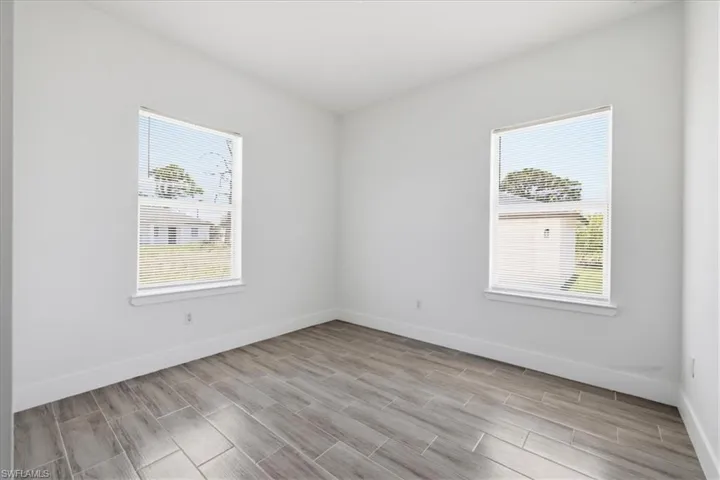 Bright room featuring two windows with horizontal blinds, neutral wall paint, white trim, and wood-look tile flooring