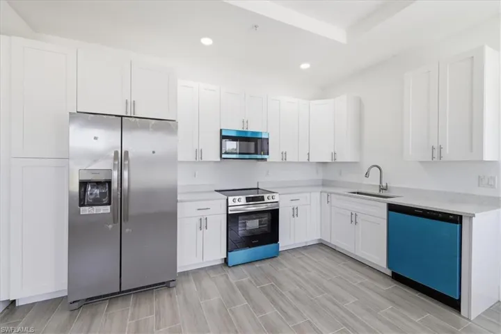 Modern kitchen featuring white shaker cabinetry, stainless steel appliances, light-toned countertops, a stainless steel sink with a gooseneck faucet, and wood-finish flooring