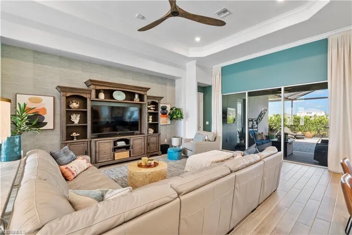 Tray ceiling with recessed lighting, large glass sliding doors, wood-finish flooring, built-in entertainment center, and a ceiling fan