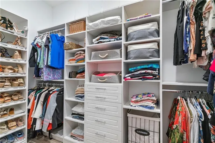 Built-in white custom closet system featuring multiple hanging rods, extensive open shelving, and integrated drawer storage