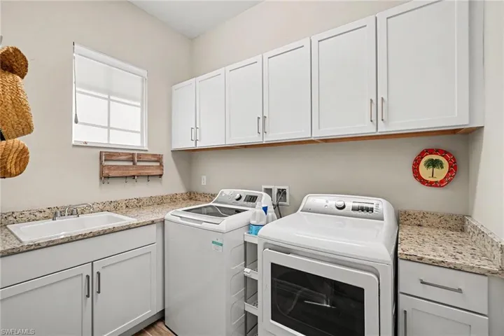 Laundry area with white cabinetry, granite-finish countertops, and a utility sink
