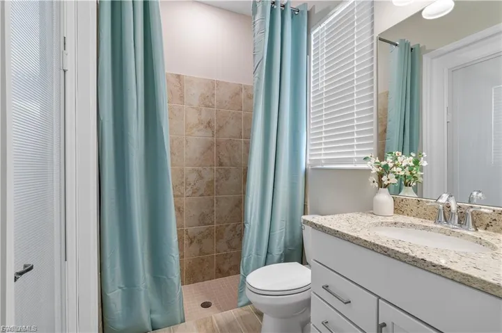 Walk-in shower with natural stone-look tiling, single vanity with light-toned countertop, and chrome fixtures