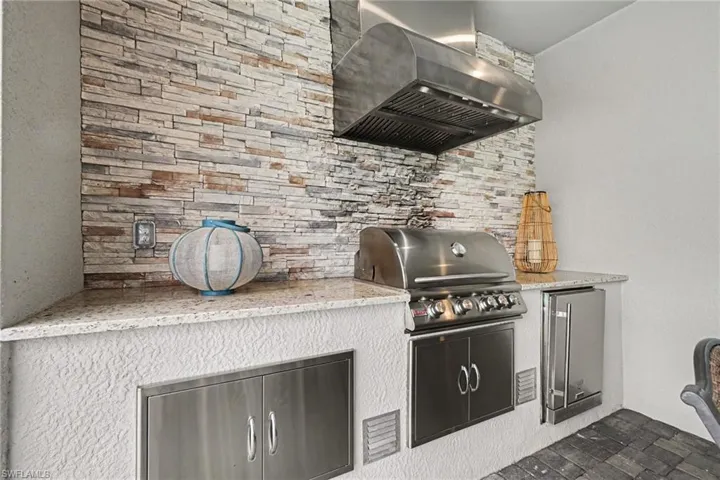 Built-in grill with a stainless steel range hood, stone veneer backsplash, and granite countertop