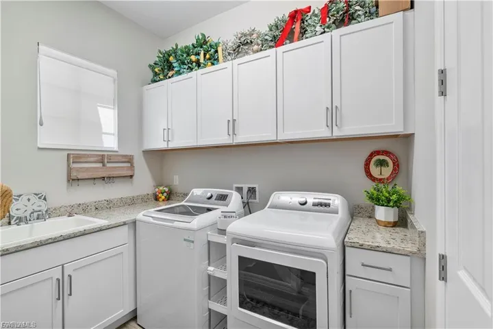 White shaker cabinetry, light-toned countertop, utility sink, and a built-in window with roller shade