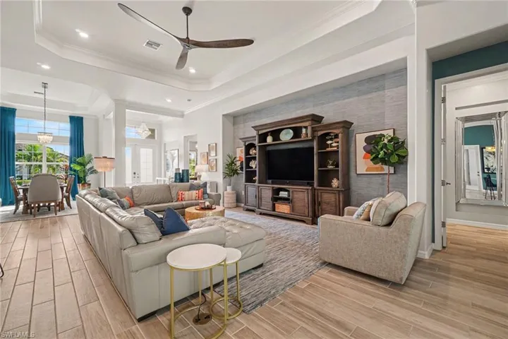 Open-concept living area with wood-finish flooring, tray ceiling, and a prominent media wall