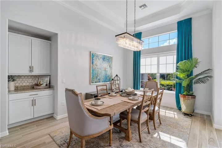 Built-in cabinetry with granite countertop and hexagonal tile backsplash, wood-finish flooring, tray ceiling, and a large window with transom