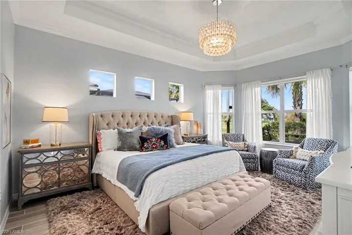 Tray ceiling with crown molding, chandelier lighting, multiple windows, wood-finish flooring, and light wall tones