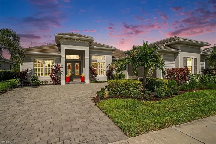 Tiled roof residence featuring a paver driveway, double entry doors, window shutters, and landscaped grounds