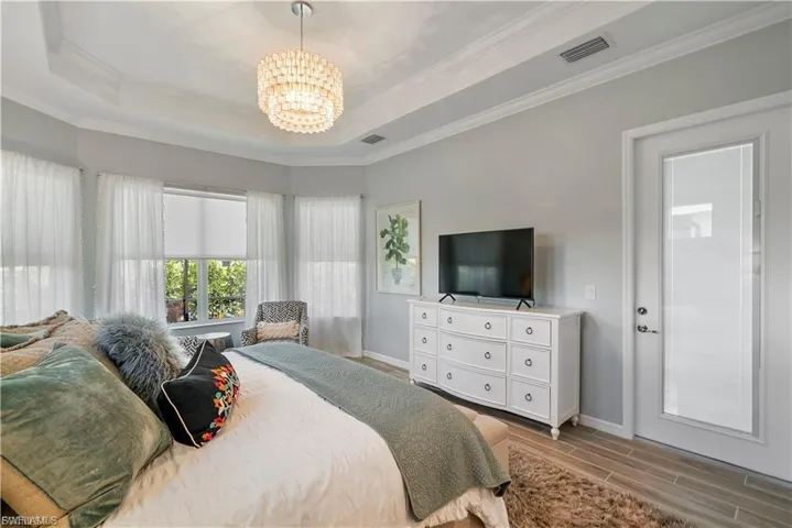Tray ceiling with crown molding, three bay windows, overhead drum chandelier, wood-look flooring, and a glass-paneled door