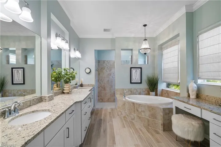 Spacious bathroom featuring dual vanities with stone countertops, a large soaking tub, and a separate tiled shower