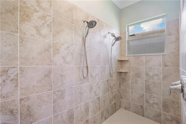 Tiled shower enclosure featuring two showerheads, an operable window, two built-in corner shelves, and a tiled shower floor