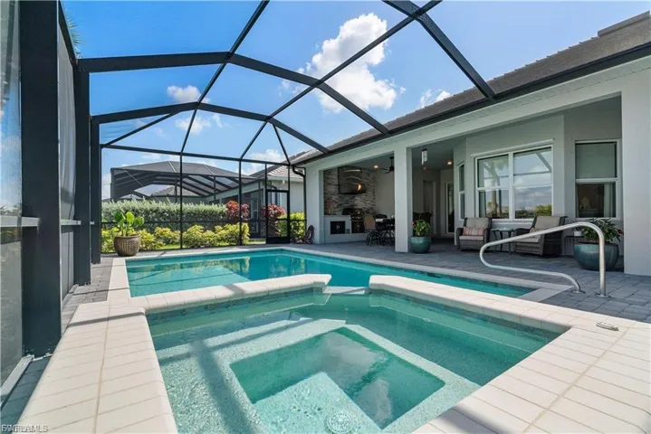 Screened outdoor living area featuring a rectangular pool, integrated spa, and paver decking