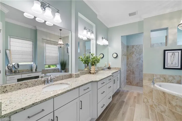Dual vanity with white cabinetry and light-toned countertops, large wall-mounted mirror, walk-in shower with tiled walls, separate soaking tub, and wood-finish flooring
