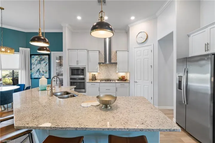 Spacious kitchen island with an undermount double sink, stainless steel appliances, white cabinetry, and recessed lighting