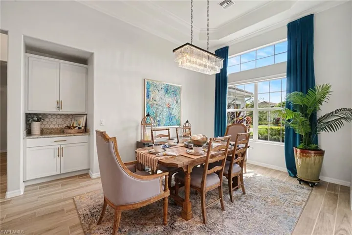 Expansive dining area featuring a tray ceiling, contemporary chandelier, large windows with upper transom panes, and wood-finish flooring