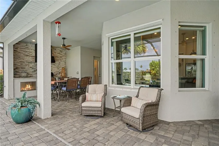 Expansive outdoor covered patio featuring a stone veneer accent wall, built-in gas fireplace, ceiling fan, and paver flooring