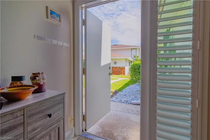 Front entrance door to townhome with sidelight and plantation shutter overlooking grassy courtyard