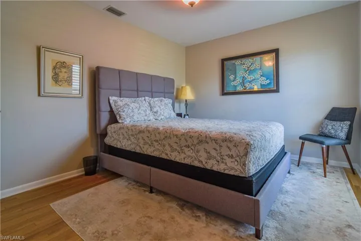 Primary bedroom with upholstered bed, warm wooden flooring, ceiling fan, impact glass window with plantation shutter