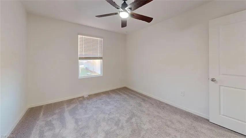 Carpeted flooring, window with blinds, ceiling fan with light, white interior door, and light-toned walls