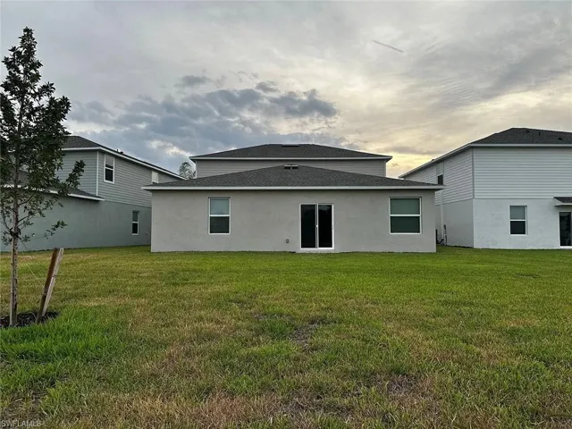 Rear exterior featuring a sliding glass door, multiple windows, and a shingled roof