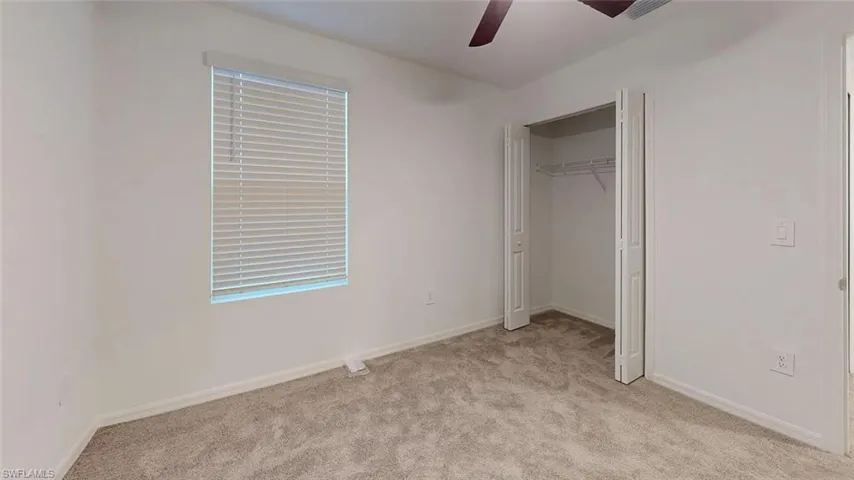 Carpeted room featuring a window with blinds, bi-fold closet doors, and a ceiling fan