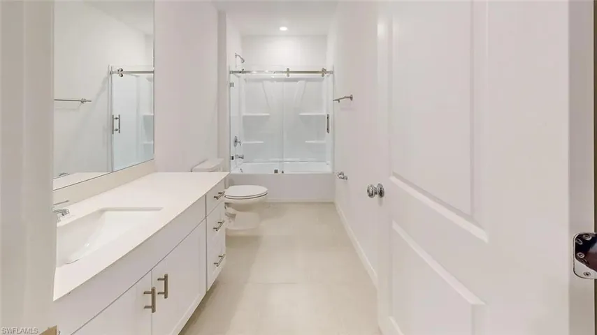 White vanity with integrated sink, expansive mirror, tile flooring, and a shower-tub combination with a sliding glass door
