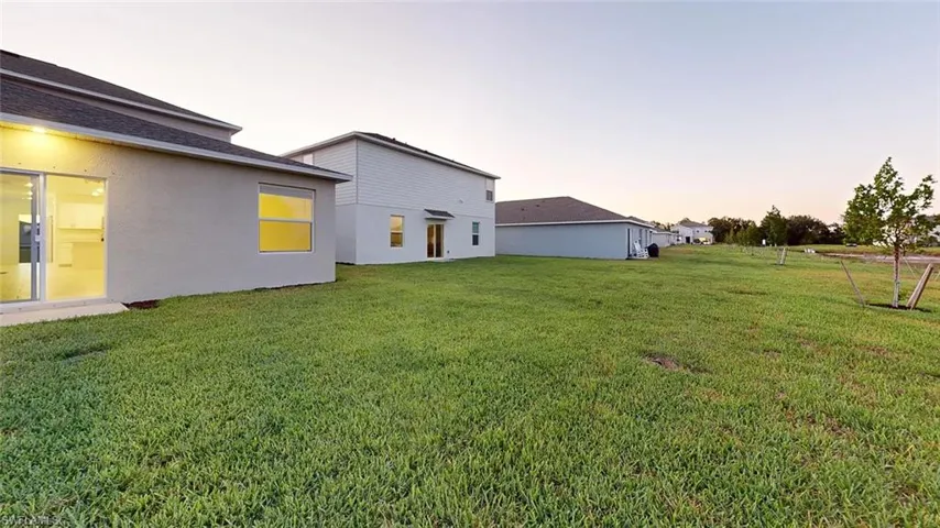 Expansive grassy yard with a concrete patio, sliding glass door, and exterior lighting