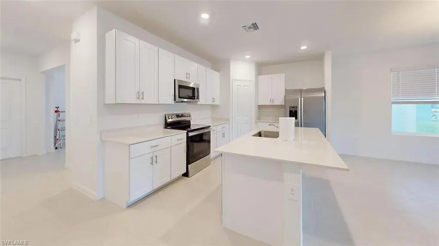 Modern kitchen featuring white shaker cabinetry, stainless steel appliances, a center island with sink, light-toned countertops, and recessed lighting