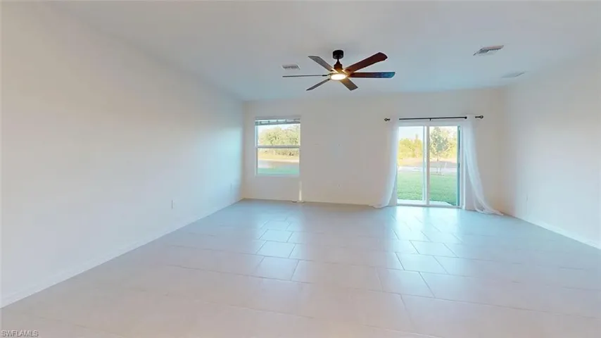 Expansive room featuring light tile flooring, a modern ceiling fan, multiple windows, and a sliding glass door