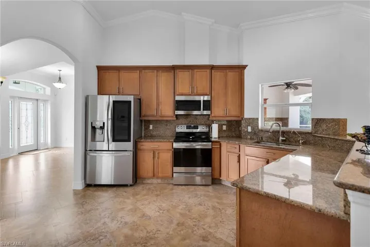 Kitchen featuring appliances with stainless steel finishes, ceiling fan, sink, stone countertops, and high vaulted ceiling