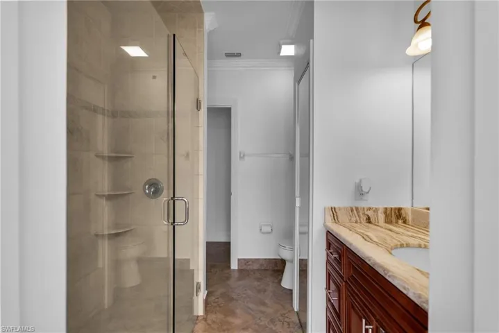 Bathroom with toilet, crown molding, a shower with shower door, and vanity