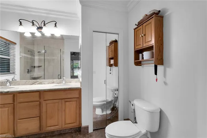 Bathroom with a shower with shower door, toilet, vanity, and crown molding