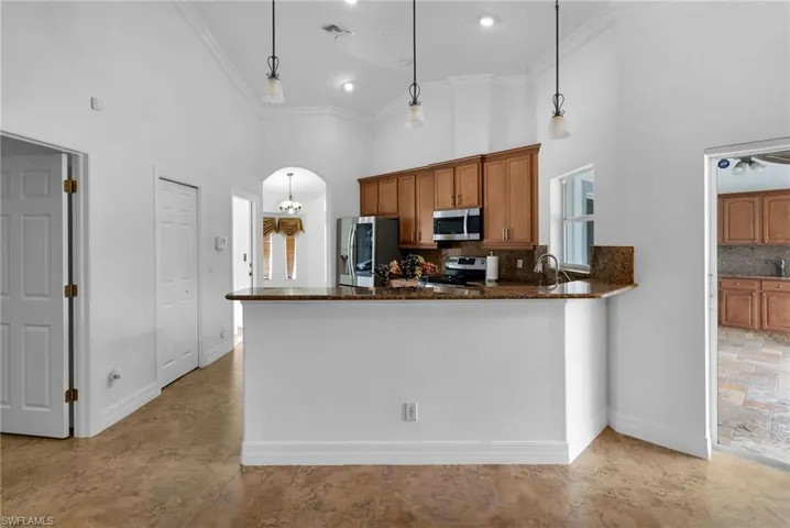 Kitchen featuring decorative light fixtures, stainless steel appliances, backsplash, and high vaulted ceiling