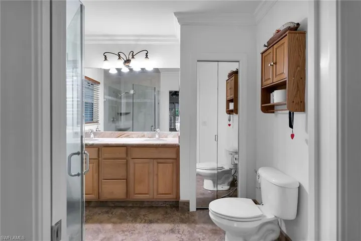 Bathroom with a shower with shower door, toilet, vanity, and ornamental molding