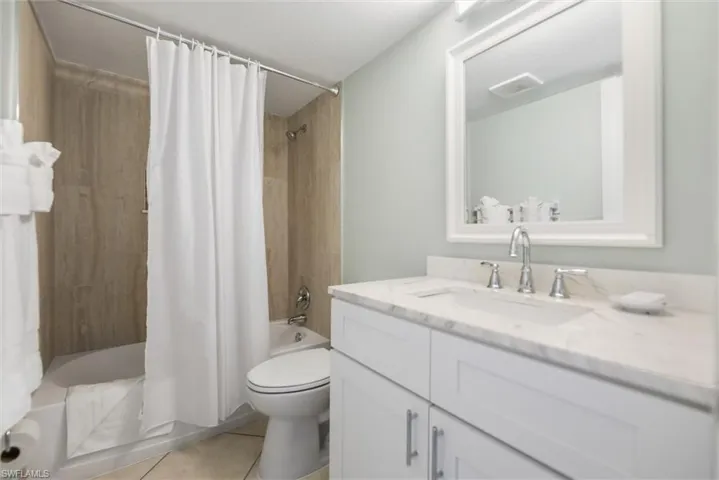 Bathroom featuring shower / bath combo with shower curtain, vanity, and light tile patterned floors