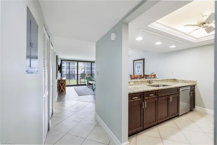 Kitchen featuring dark brown cabinets, light stone counters, light tile patterned floors, and dishwasher
