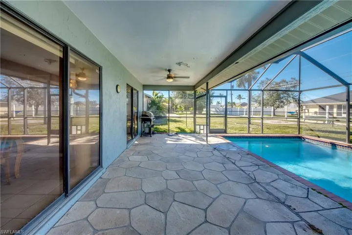 View of pool with glass enclosure, ceiling fan, and a patio area