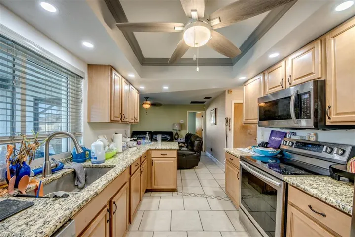 Kitchen featuring light brown cabinetry, sink, appliances with stainless steel finishes, and a tray ceiling