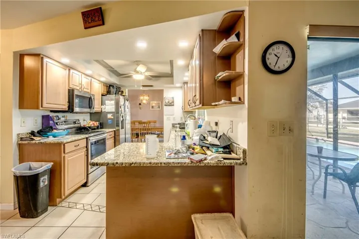 Kitchen with ceiling fan, light stone countertops, a raised ceiling, kitchen peninsula, and appliances with stainless steel finishes