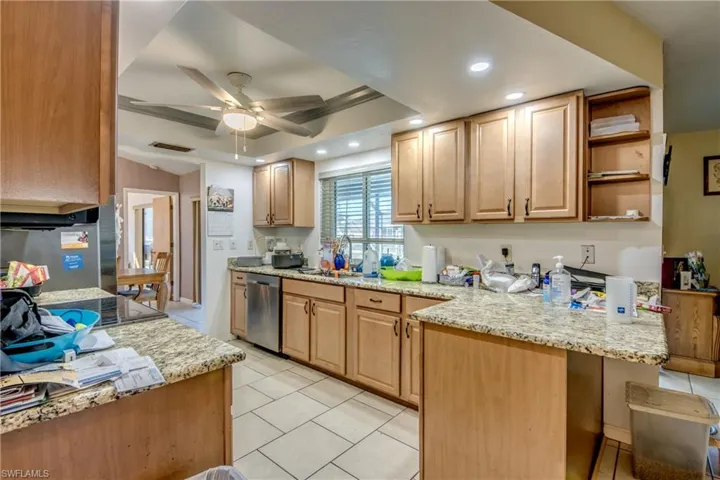 Kitchen featuring ceiling fan, sink, light stone countertops, stainless steel dishwasher, and a tray ceiling