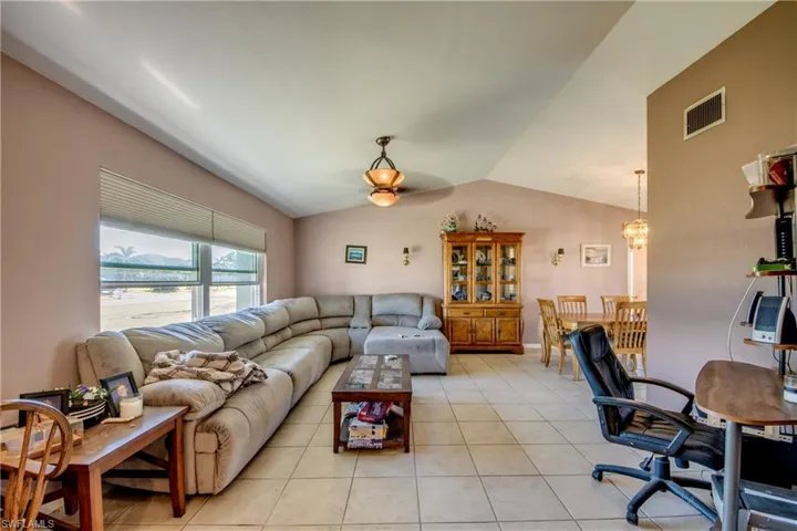 Living room with ceiling fan with notable chandelier, lofted ceiling, and light tile patterned floors