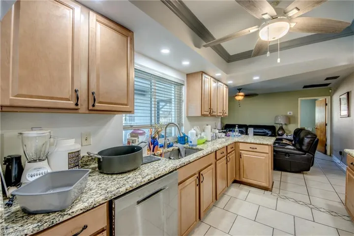 Kitchen with sink, light stone counters, stainless steel dishwasher, crown molding, and light tile patterned floors