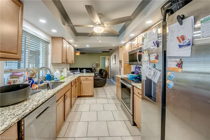 Kitchen featuring a raised ceiling, sink, ceiling fan, appliances with stainless steel finishes, and light stone counters