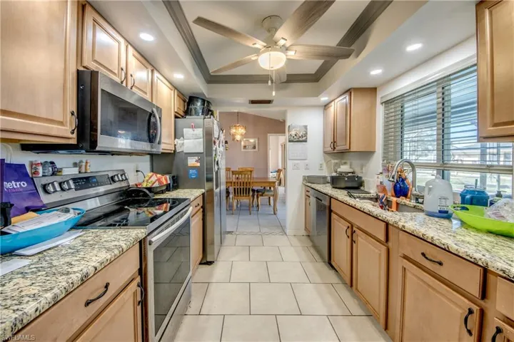 Kitchen featuring crown molding, sink, ceiling fan, appliances with stainless steel finishes, and a tray ceiling