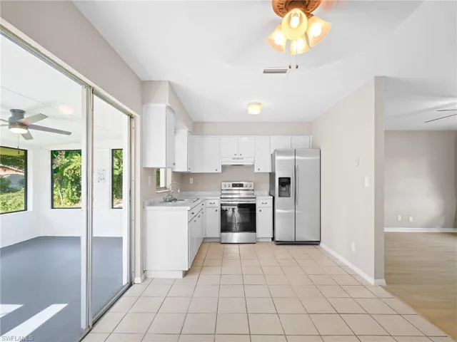 Kitchen with ceiling fan, stainless steel appliances, light countertops, light tile patterned floors, and white cabinetry