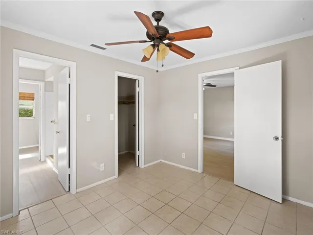 Unfurnished bedroom with ornamental molding, light tile patterned flooring, a spacious closet, and a ceiling fan